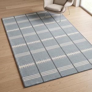 Könnte beinhalten: Ein rechteckiger Teppich mit hellblauer Grundfläche und einem Gittermuster aus dunkelgrauen Linien. Das Design umfasst horizontale weiße Streifen sowie kleine, sich wiederholende weiße rechteckige Akzente in den blauen Gitterfeldern.