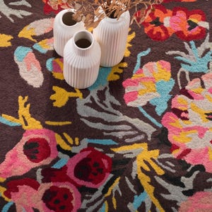 Overhead detail shot of a floral rug with spools of colorful wool yarn resting on top to highlight craft materials.
