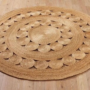 May include: A round, natural fiber rug with a circular pattern of woven loops. The rug has a light brown color and a textured surface.