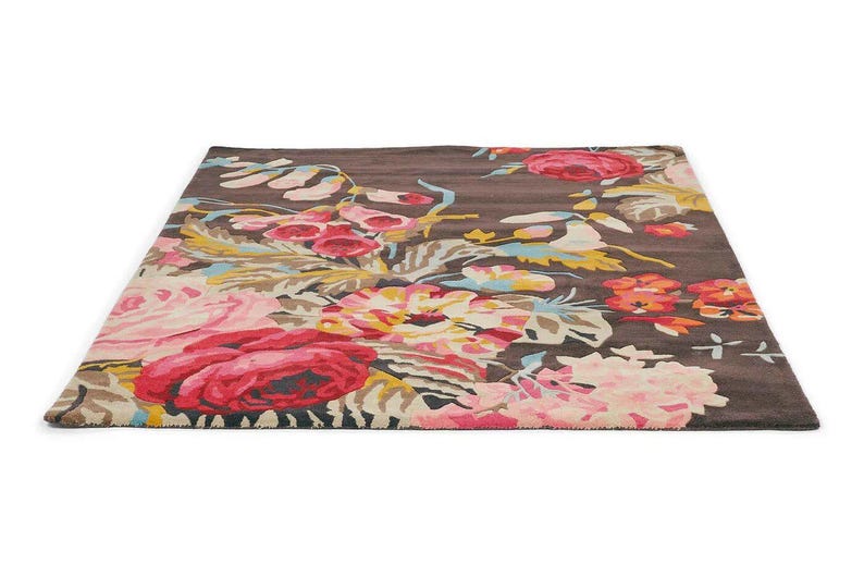 Colourful wool area rug styled beneath a neutral sofa in a contemporary living room.Ground-level perspective photograph of a dark brown wool area rug with pink and red floral patterns extending across the room.