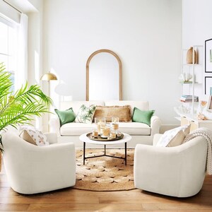May include: A white living room with two white armchairs, a white sofa, a coffee table with candles, a large green plant, and a wooden arched mirror.
