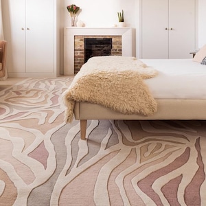 Könnte beinhalten: Ein Schlafzimmer mit einem gemusterten Teppich in Beige-, Rosa- und Grautönen. Das Design des Teppichs ähnelt einem Zebra-Print. Ein Bett mit einer cremefarbenen Bettdecke und einem gemusterten Kissen befindet sich im Raum. Ein Sofa und ein Kamin sind ebenfalls zu sehen.