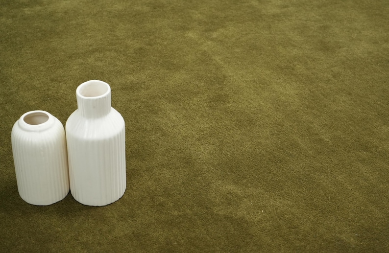 Peut inclure: Deux vases en c&eacute;ramique blanche avec des d&eacute;tails c&ocirc;tel&eacute;s verticaux. L'un est cylindrique avec une ouverture &eacute;troite, l'autre est en forme de bouteille plus haute avec une ouverture plus large. Sur fond vert olive textur&eacute;.