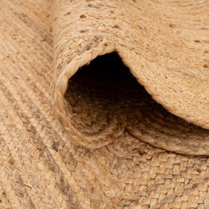 K&ouml;nnte beinhalten: Nahaufnahme eines Naturfaser-Teppichs aus Jute. Der Teppich ist in einem engen, strukturierten Muster gewebt und hat eine nat&uuml;rliche, erdige Farbe.