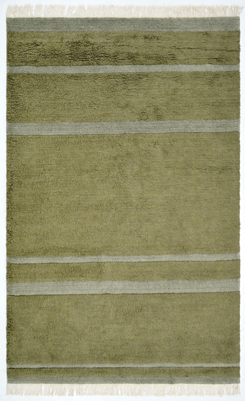 Pode incluir: Um tapete retangular verde-oliva com listras cinza horizontais. O tapete tem uma superf&iacute;cie texturizada e franjas nas bordas superior e inferior. Um item de decora&ccedil;&atilde;o para casa.