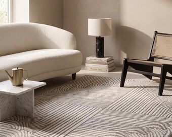 May include: A rectangular area rug featuring a repeating geometric pattern of raised, dark gray lines on a light cream background. The design consists of intersecting linear segments and curved arcs that create a textured, high-contrast visual effect.