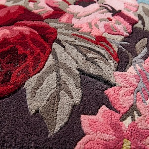 Extreme close-up photograph of a hand-tufted wool rug detailing the carved lines, rich red and pink yarn fibers, and cut-pile texture of the floral pattern.