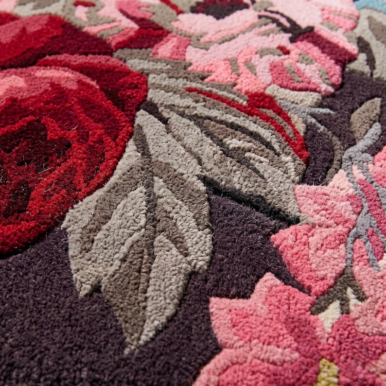 Extreme close-up photograph of a hand-tufted wool rug detailing the carved lines, rich red and pink yarn fibers, and cut-pile texture of the floral pattern.