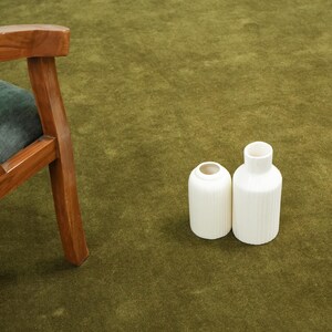 Peut inclure: Deux vases en c&eacute;ramique blanche avec des d&eacute;tails c&ocirc;tel&eacute;s verticaux sur une surface verte. Une chaise en bois avec un coussin vert est partiellement visible &agrave; gauche. Les vases ont un design minimaliste.