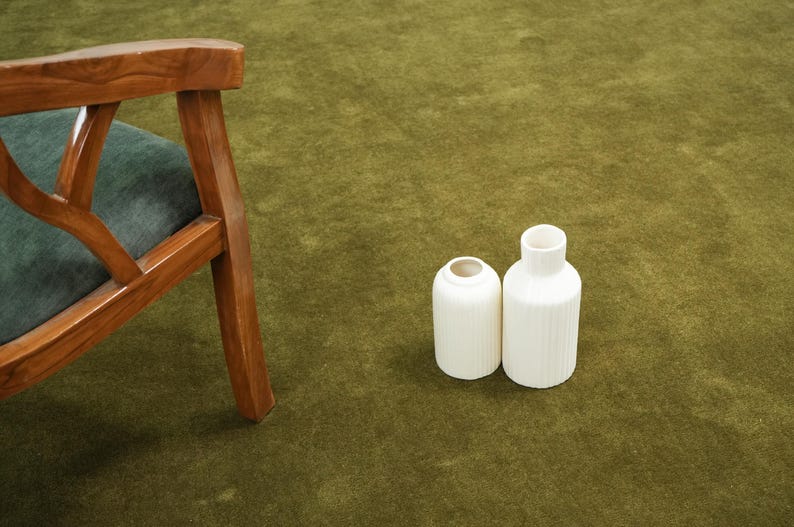 Peut inclure: Deux vases en c&eacute;ramique blanche avec des d&eacute;tails c&ocirc;tel&eacute;s verticaux sur une surface verte. Une chaise en bois avec un coussin vert est partiellement visible &agrave; gauche. Les vases ont un design minimaliste.