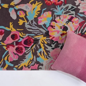 Partial top-down view of a floral hand-tufted rug styled on a light wooden floor with a dusty pink accent pillow placed on top. Summer Bloom multicolor floral rug displayed as a statement carpet for a living room or bedroom