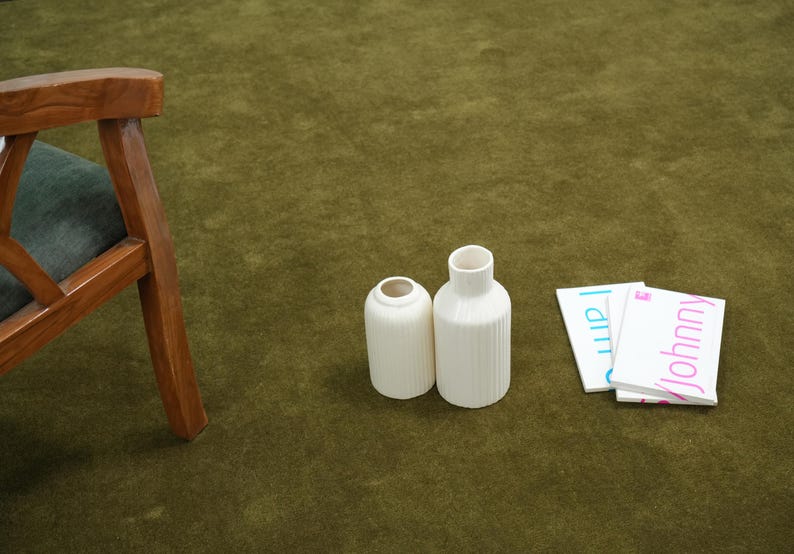 Peut inclure: Deux vases en c&eacute;ramique blanche avec des d&eacute;tails c&ocirc;tel&eacute;s et une petite pile de cartes blanches avec les noms "Johnny" et "I am" imprim&eacute;s dessus. Les articles sont sur une surface verte.