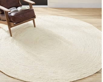 May include: A white round jute rug with a woven texture. The rug has a natural, off-white color and a slightly raised center.