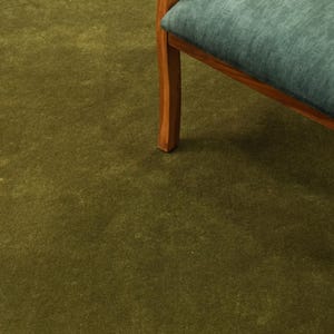 Peut inclure: Un morceau de tapis vert olive avec une chaise en bois. La chaise a un coussin bleu sarcelle et un cadre en bois. Le tapis est de couleur unie et recouvre le sol.