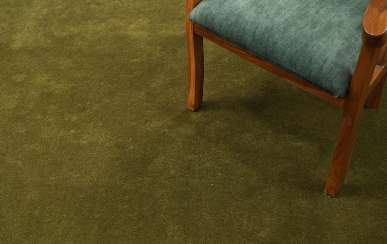 Peut inclure: Un morceau de tapis vert olive avec une chaise en bois. La chaise a un coussin bleu sarcelle et un cadre en bois. Le tapis est de couleur unie et recouvre le sol.