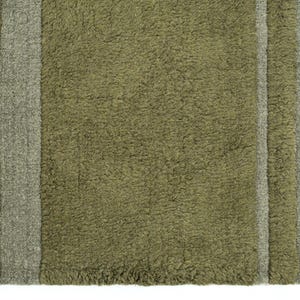 Pode incluir: Close-up de um tapete verde-oliva texturizado com duas listras cinza verticais. O tapete tem uma apar&ecirc;ncia felpuda e uma franja na borda direita. Este tapete &eacute; adequado para decora&ccedil;&atilde;o de casa.