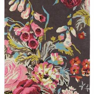 Top-down view of a rectangular hand-tufted wool rug featuring a dark brown background filled with vibrant pink roses, foxgloves, and botanical leaves. Full top view of the Summer Bloom floral rug with pink, aqua, mustard and green botanical details.