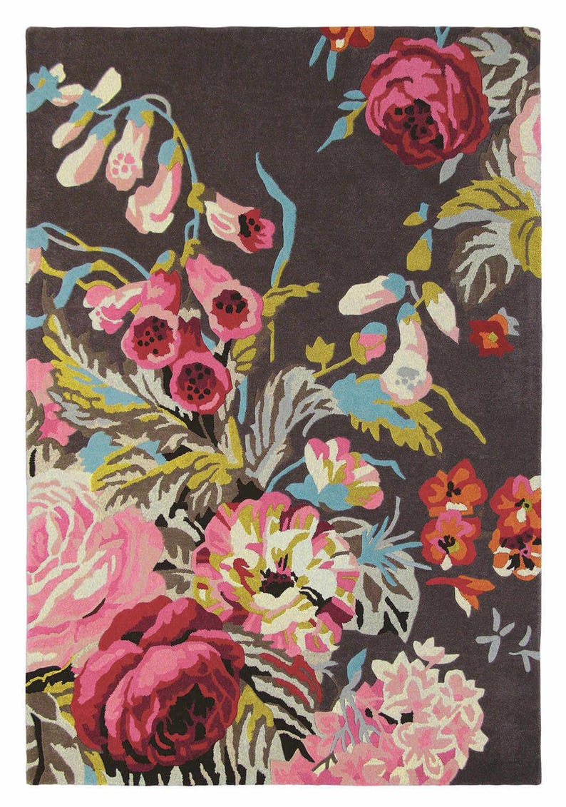 Top-down view of a rectangular hand-tufted wool rug featuring a dark brown background filled with vibrant pink roses, foxgloves, and botanical leaves. Full top view of the Summer Bloom floral rug with pink, aqua, mustard and green botanical details.