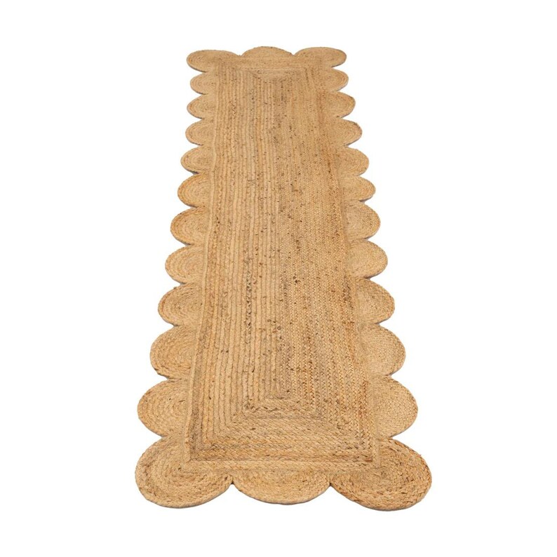 K&ouml;nnte beinhalten: Ein Naturfaser-Teppich mit einem gewellten Rand. Der Teppich ist aus Jute und hat eine hellbraune Farbe.