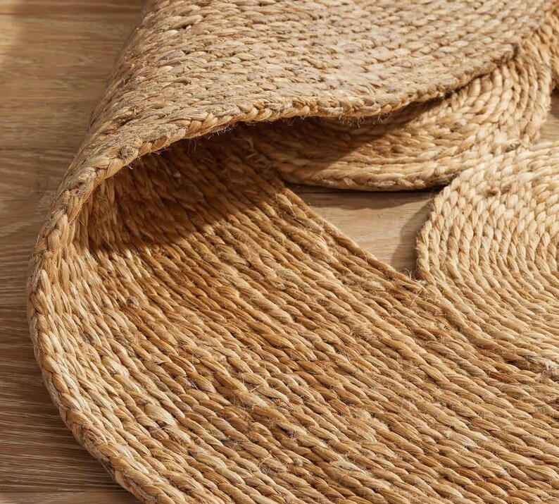 May include: A natural fiber rug made from jute, featuring a circular design with a woven texture. The rug is a light brown color and has a slightly rough surface.