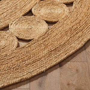 May include: A round, natural fiber rug with a woven design featuring circles of varying sizes. The rug is made of a natural material, such as jute or sisal, and has a warm, earthy tone.