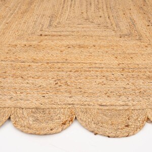 K&ouml;nnte beinhalten: Ein Naturfaser-Teppich mit einem gewellten Rand. Der Teppich ist aus Jute und hat eine hellbraune Farbe.