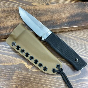 May include: A stainless steel fixed blade knife with a black textured handle and a tan sheath. The knife blade is silver and the sheath has multiple eyelets along the edge. A black cord is attached to the sheath.