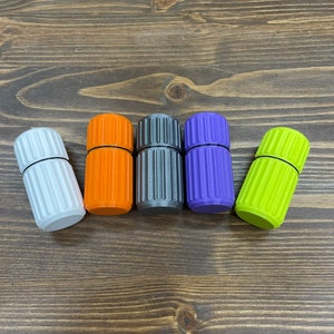 Puede incluir: Cinco pequeños contenedores cilíndricos con lados acanalados. Los contenedores son blancos, naranja, grises, morados y verdes.