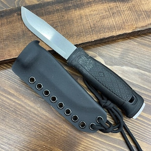 Pode incluir: Uma faca de sobrevivência com uma lâmina prateada e um cabo preto texturizado. A faca é combinada com uma bainha de couro preta com ilhós e um cordão preto. A faca foi projetada para uso ao ar livre.
