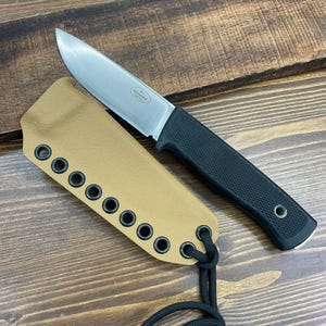 May include: A stainless steel fixed-blade knife with a black handle and a tan sheath. The knife is lying next to its sheath on a wooden surface. The sheath has multiple eyelets and a black cord.