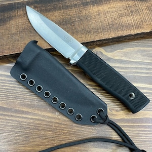 May include: A stainless steel knife with a black textured handle and a black leather sheath. The knife has a silver blade and is laying next to its sheath on a wooden surface. The sheath has multiple eyelets and a black cord.