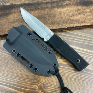May include: A stainless steel knife with a black handle and a black sheath. The knife blade is silver and the handle has a textured grip. The sheath has multiple eyelets and a cord for securing the knife. The knife is approximately 8 inches long.