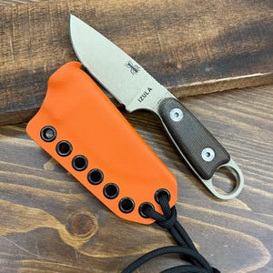 May include: A small, fixed-blade knife with a textured handle and a silver blade. The blade has a spider logo and the word "IZULA" printed on it. It is paired with an orange sheath with black eyelets and a black lanyard.