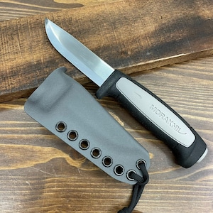 May include: A stainless steel blade knife with a black and gray handle and a gray sheath. The knife is labeled "MORAKNIL" on the handle. The sheath has multiple eyelets and a black cord.