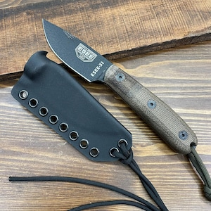 May include: A black ESEE-3 knife with a brown handle and a black sheath. The knife blade has the text "ESEE-3" and the ESEE logo. The sheath is black with multiple eyelets and a black cord.
