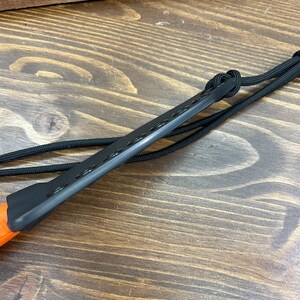 Puede incluir: Un iniciador de fuego negro con una serie de agujeros a lo largo del borde superior. El mango es naranja y el cord&oacute;n es negro. El iniciador de fuego est&aacute; dise&ntilde;ado para uso en exteriores.