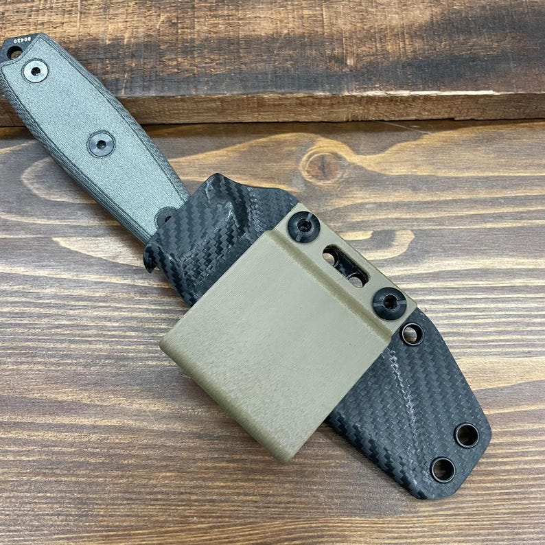Puede incluir: Un cuchillo negro y verde con una funda de fibra de carbono. La funda tiene un clip de color beige y tornillos negros.