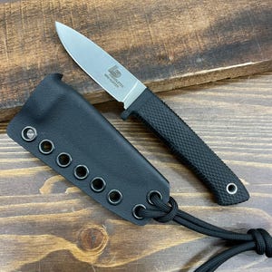 May include: A small, silver-bladed knife with a black textured handle and a black sheath. The knife has the text "LD TINDLETON MINI HUNTER" printed on the blade. The sheath has multiple eyelets and a black cord.
