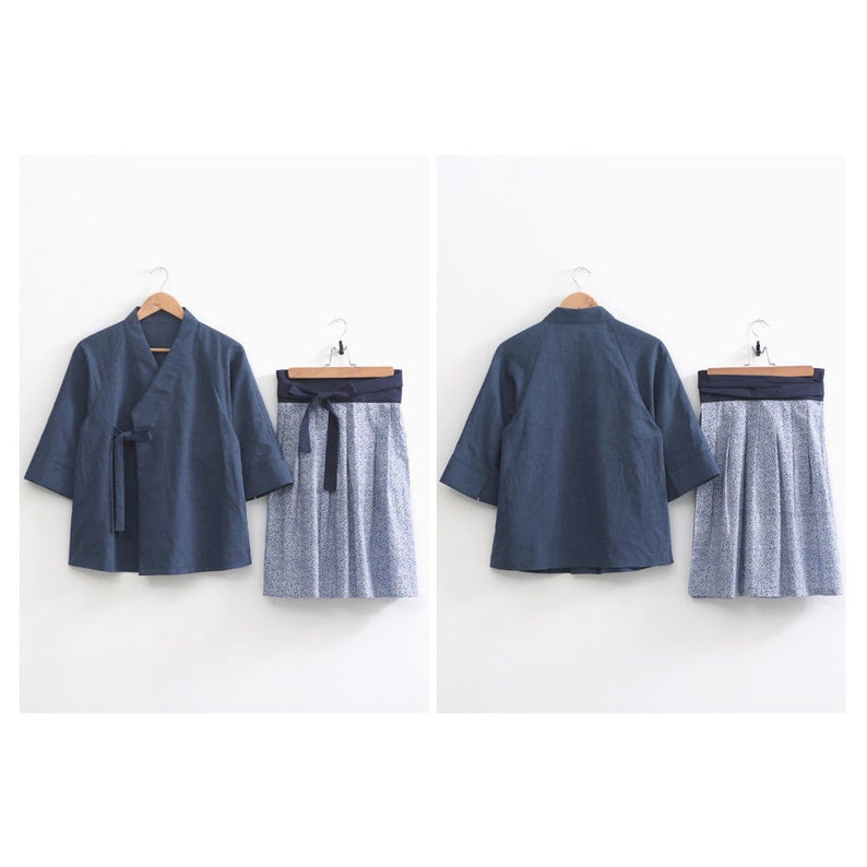 May include: A navy blue traditional Korean hanbok set, including a jacket with a tie closure and a skirt with a floral pattern. The outfit is displayed on wooden hangers against a white background.