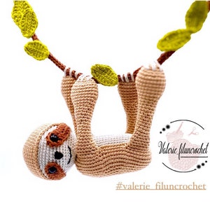 Peut inclure: Un paresseux en crochet suspendu à une branche avec des feuilles vertes. Le paresseux est brun et a un ventre blanc. Le paresseux a un visage souriant avec des yeux noirs et un nez brun. Le texte "#valerie_filuncrochet" est visible sur l'image.