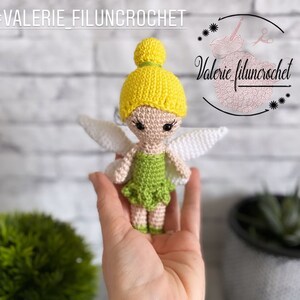 Peut inclure: Une poupée fée crochetée avec un bonnet jaune, une robe verte et des ailes blanches. La poupée est tenue dans une main. Le texte "#VALERIE_FILUNCROCHET" est en haut à gauche. Le logo "Valerie filuncrochet" est en haut à droite.