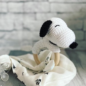 May include: White crocheted dog toy with black ears and a wooden teething ring. The toy is lying on a white muslin blanket with black stars. A clear pacifier is also visible in the image. The text #VALERIE FILUNCROCHET is written on the blanket.