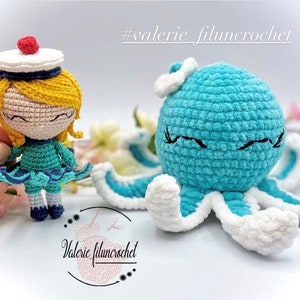 May include: A crocheted blue octopus with white accents and a crocheted doll wearing a blue and white sailor hat and a blue dress. The doll has yellow hair and closed eyes. The octopus has closed eyes and a white cloud on its head. The image includes the text #valerie_filuncrotchet.
