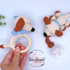 May include: Two crocheted dog toys. One is a rattle with a wooden ring and the other is a pacifier clip. Both are cream colored with brown ears and a blue bow.