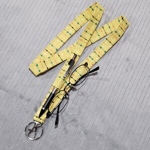 May include: A yellow lanyard with a repeating pattern of green, pink, and white dots. A black pen and glasses are attached to the lanyard.
