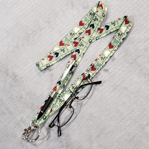 May include: A green lanyard with a white and red heart pattern. A pen and glasses are attached to the lanyard.