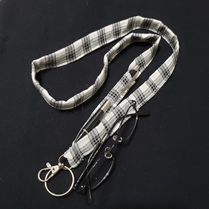 May include: A black and white plaid lanyard with a silver clip and a black pen and glasses tucked into it.