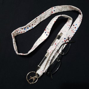 May include: A white lanyard with red and blue stars printed on it. The lanyard has a silver pen and black glasses attached to it.