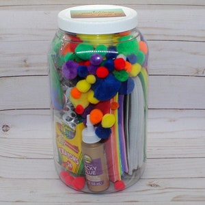 May include: A clear plastic jar filled with colorful craft supplies, including pom-poms, pipe cleaners, construction paper, googly eyes, crayons, and glue. The jar has a white lid with a label that reads "Ultimate Craft Kit".