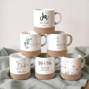 Könnte beinhalten: Sechs weiße Keramikbecher mit Korkböden. Jeder Becher hat ein anderes Design und einen anderen Text. Die Designs umfassen ein Blumenmuster, ein Blattmuster und handschriftlichen Text. Der Text umfasst "Ja", "Lisa & Nico", "Du. Ich. Passt. Franz", "Für Dich", "Mr. & Mrs" und "Anne & Bene".